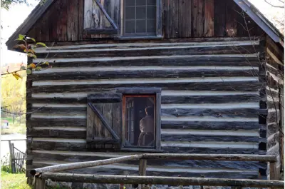 exterior log cabin image, looking in the window, figure of woman inside. building titled Maw House